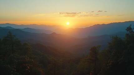 Fototapeta premium Golden sunset over mountain range. Smoky hazy light bathes the distant peaks in warm hues, while the foreground shows lush green trees.