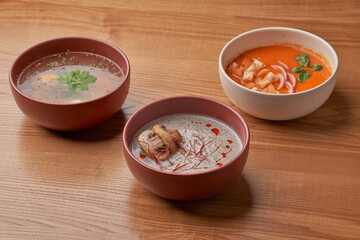 A variety of soups, including a clear broth, a creamy mushroom soup, and a vibrant tomato soup, served in individual bowls.