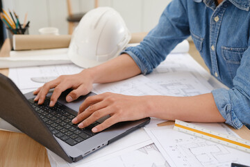 Architect and engineer working on blueprints using a laptop at a desk