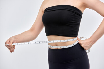 An Asian woman is on a diet and measuring her waist size using a tape measure.	
