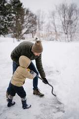 Man with his son shoveling snow in the driveway after a winter storm