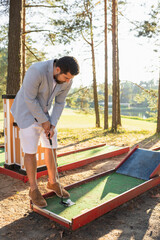 Mini golf player holding golf club next to ball ready to strike