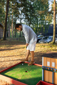 Stylish young adult man playing mini golf on a forest court