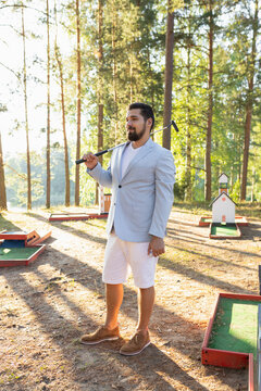 Portrait of young adult mini golf player with club on court in forest