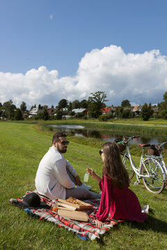 Couple having picnic with pizza and bicycles on glass by the river