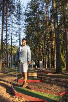 Handsome mini golf player standing on court in forest after strike