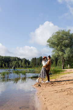 Cute couple embracing by the lake on a sunny day against blue sky