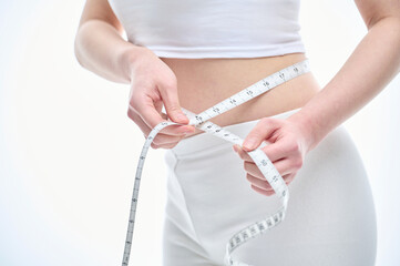 An Asian woman is on a diet and measuring her waist size using a tape measure.	
