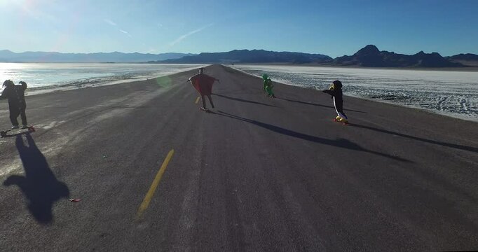 Cinematic drone shot soaring over group of people in costumes on skateboards riding on empty desert road