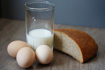 A glass of milk, bread and eggs on the table.