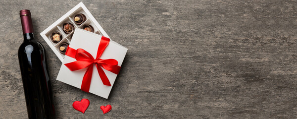 Bottle of red wine on colored background for Valentine Day with gift and chocolate. Heart shaped...