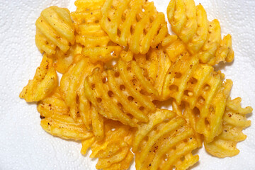 waffle criss cross fries,  freshly fried, on kitchen paper towel absorbing the grease. Fast food background backdrop.