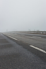 Fototapeta premium Empty highway in the fog. Bad weather on the road. Road on foggy day in perspective with copy space. Driving conditions concept. Ghostly misty road. Caution and danger on the road. Moody weather