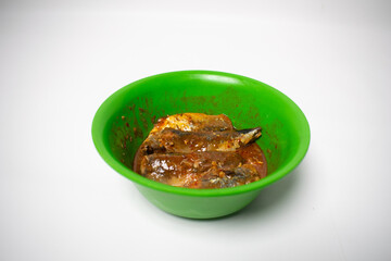 Green plastic bowl containing canned sardines with tomato sauce. The background is white.