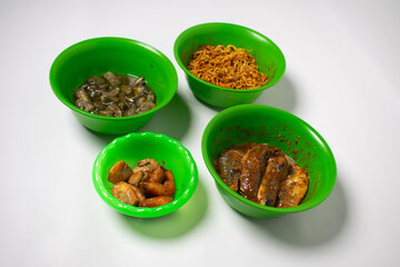 The green plastic bowl contains green eggplant, sardines, fried shrimp and fried noodles. The background is white.