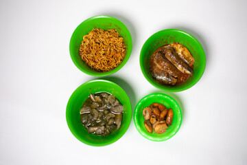 The green plastic bowl contains green eggplant, sardines, fried shrimp and fried noodles. The background is white.