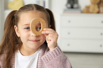 Learning alphabet. Little girl with wooden letter O indoors, space for text
