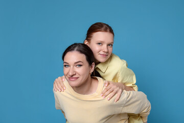 Portrait of beautiful mother with teenage daughter on light blue background