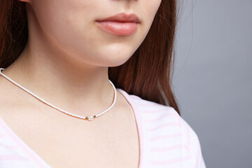 Teenage girl wearing stylish necklace on grey background, closeup