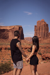 Young tourist couple holding hands and unrecognizable looking at the formations of Monument Valley, in the United States.