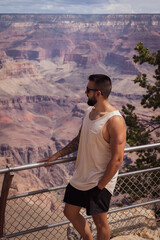 Young male tourist leaning on the fence overlooking the breathtaking Grand Canyon of the Colorado River in the United States.
