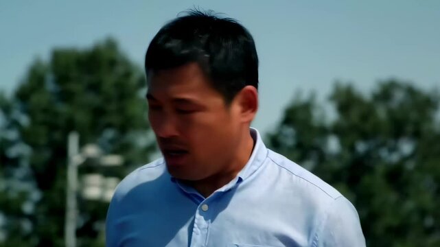 屋外で汗を拭き誰かと話すアジアの中年男性