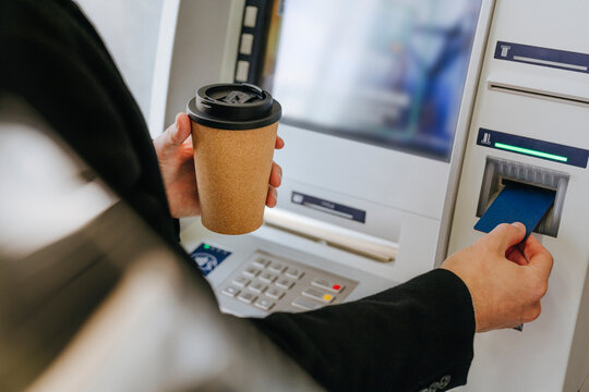 Man holding coffee and using ATM machine