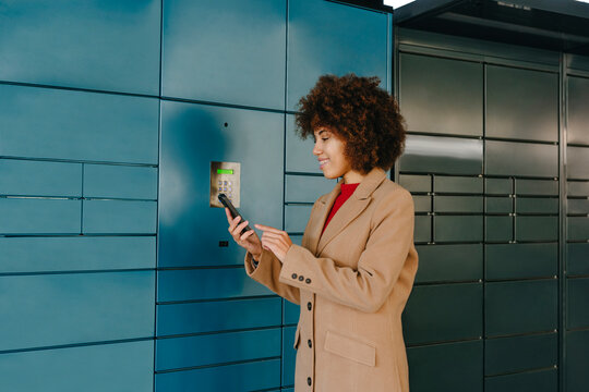 Happy businesswoman using smart phone near locker at parking lot