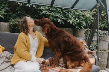 Woman sitting on swing and kissing dog at back yard