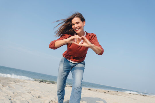 Smiling woman making heart shape with hand at beach