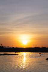 Golden sunset over a tranquil shore with silhouetted fishing boats and calm reflective waters.