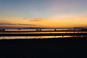 Stunning sunset over a tranquil beach with silhouetted fishing boats and distant islands.