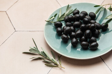 Black olives served on ceramic plate with olive branches on tiled surface