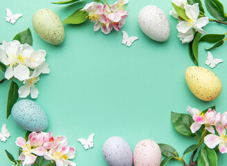 Easter eggs and spring flowers creating a frame on a turquoise background