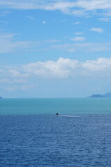 Obraz premium Serene tropical seascape with mountains under a bright blue sky and fluffy white clouds