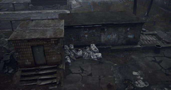 An abandoned area shows crumbling buildings, overgrown weeds, and piles of trash. The atmosphere conveys a sense of neglect, with remnants of urban life scattered around.