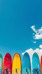 Row of vibrant surfboards against bright blue sky with fluffy white clouds.