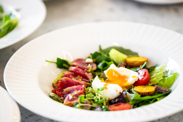 A vibrant salad featuring fresh greens, sliced meat, cherry tomatoes, and a perfectly poached egg. Presented in an elegant bowl, it's a delicious and healthy meal option.