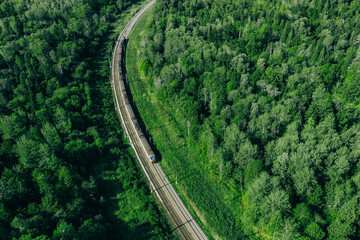 Aerial drone view of train in beautiful green summer forest. Long commuter train moving to railway...