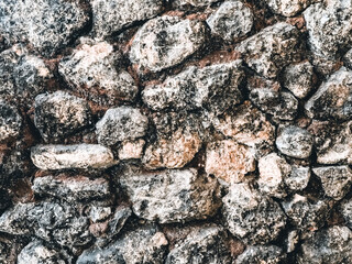 A close-up view of a rugged stone wall, featuring a mix of dark and light stones with a weathered texture