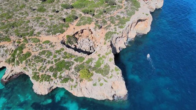 Explore the stunning cliffs and vibrant blue waters of Cala Varques in Majorca. This picturesque location features a serene boat passing by, showcasing nature's beauty.