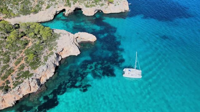 Experience the crystal-clear waters and rugged coastline of Cala Varques near Porto Cristo. Sailboats glide through beautiful bays surrounded by natural beauty and tranquility.