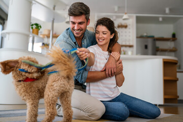 Portrait of happy multiracial couple scratching their pet dog, sitting on floor at home. Adopted pet