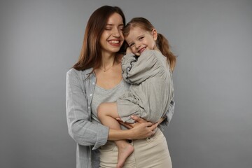 Happy mother with her cute little daughter on grey background