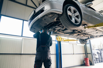 Serviceman checks car suspension on a column lift in car service