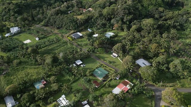 Aerial panoramic overview of quiet South Pacific neighborhood with rural homes and farmlands atb ase of mountains