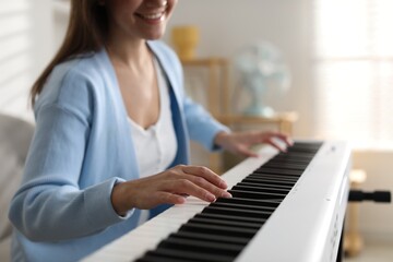 Woman playing synthesizer indoors, closeup. Electronic musical instrument