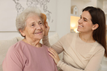 Granddaughter brushing her grandmother with comb at home. Elderly care