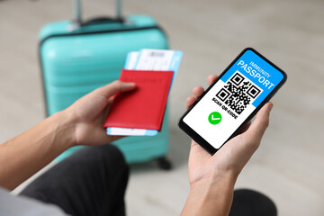 Tourist with passport, flight tickets and mobile phone indoors, above view. Immunity passport app with QR code on device screen