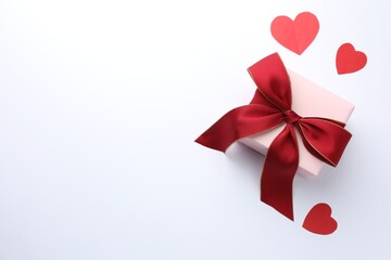 Gift box with red bow and paper hearts on white background, flat lay. Space for text